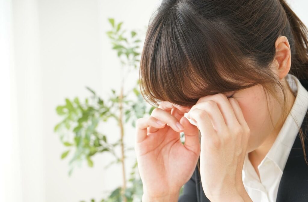 A woman rubbing her eyes with both hands.