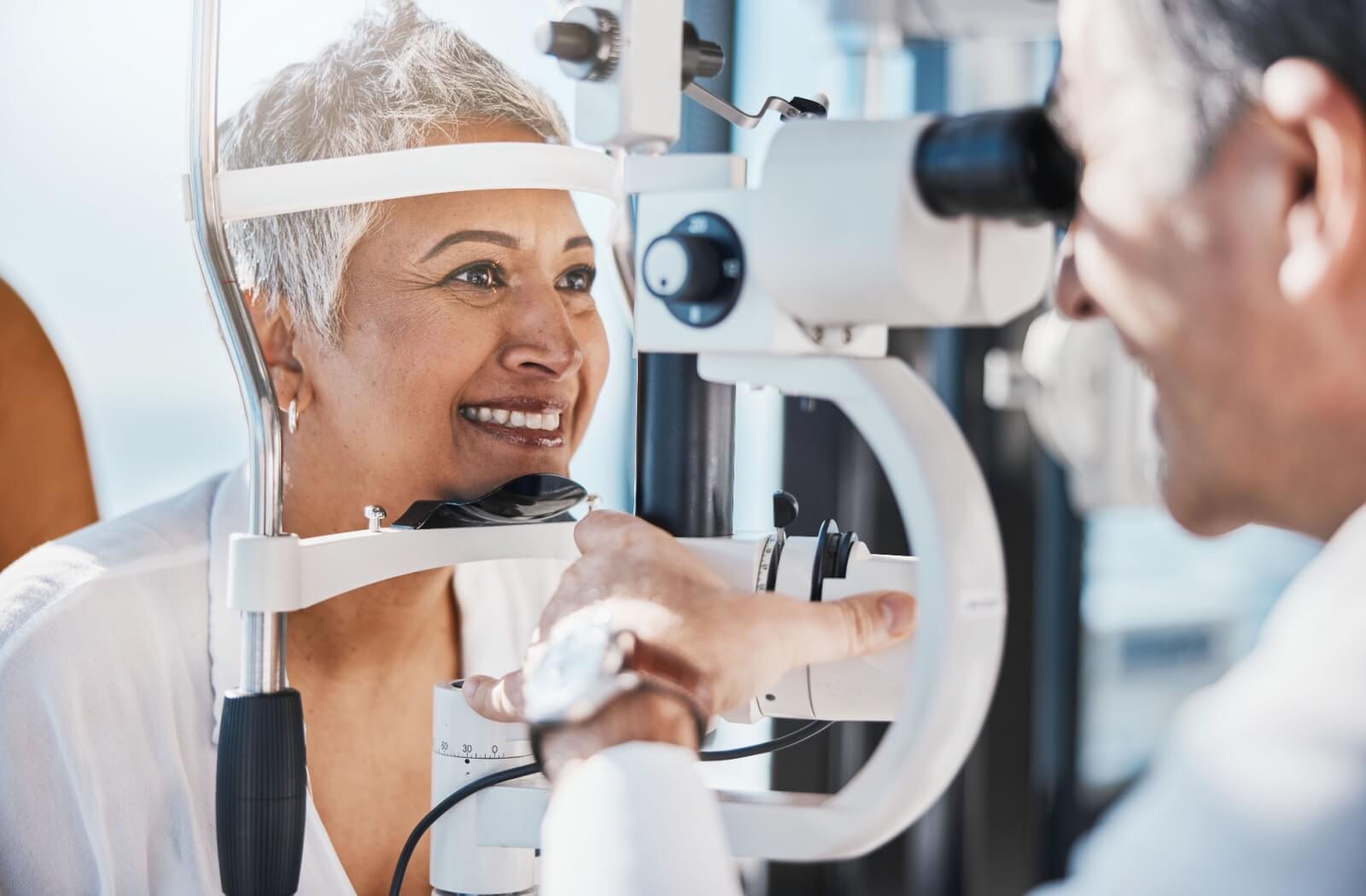 A smiling senior woman having her eyes examined in an optometry clinic by a male optometrist.