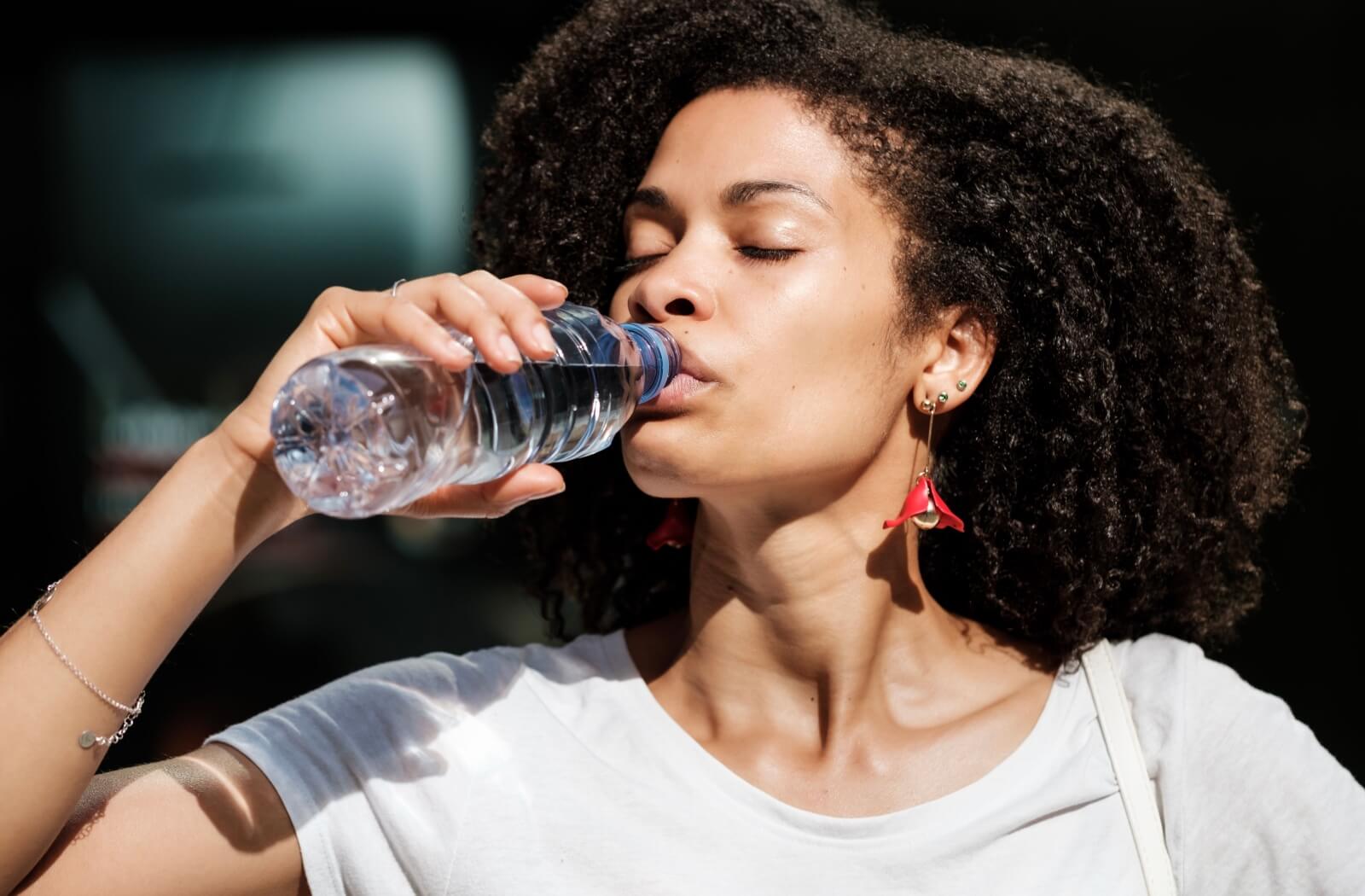 A woman drinking water from a plastic bottle.