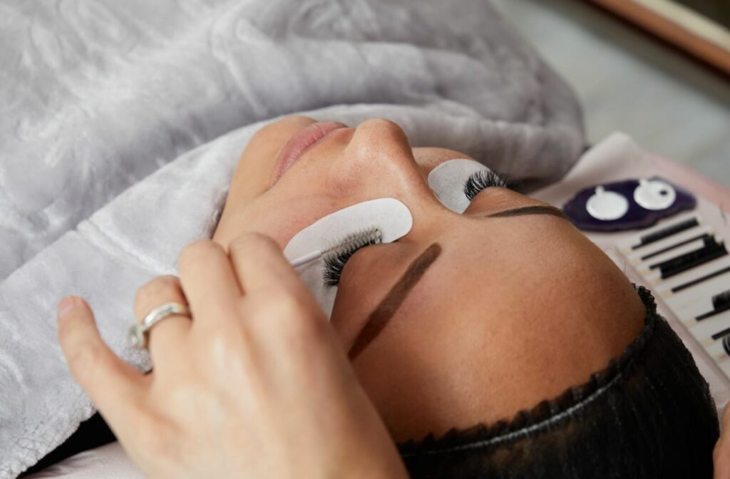 Close-up of a patient with closed eyes getting eyelash extensions, the salon tech carefully applying a solution