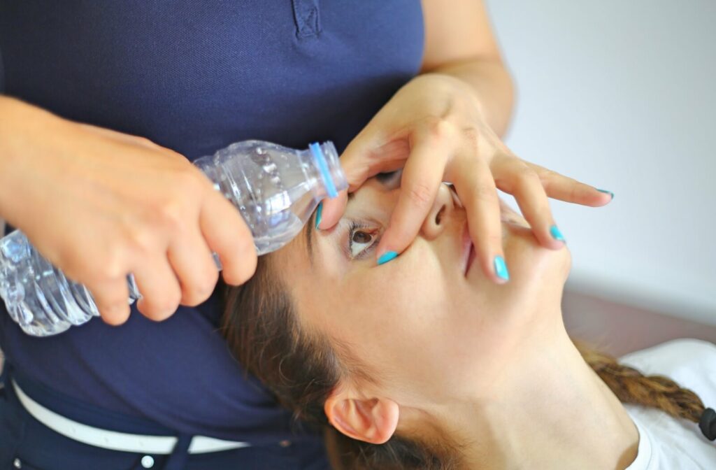 A parent holds open the eye of a teenager, holding bottled water poised over their eye to flush it out