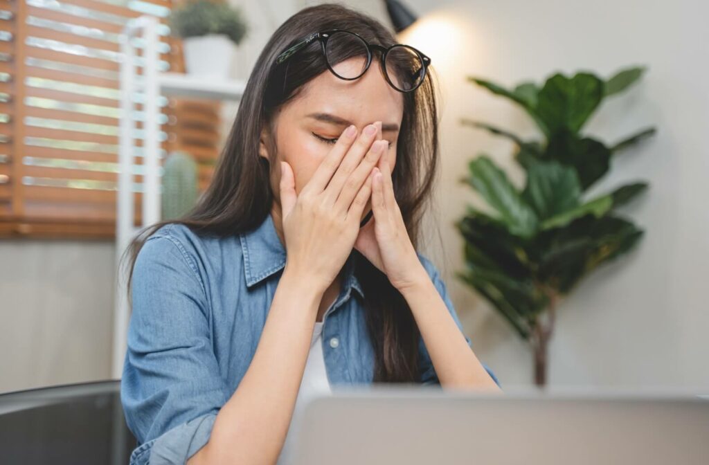 A woman in an office pushing her glasses up to rub her eyes with her fingers.