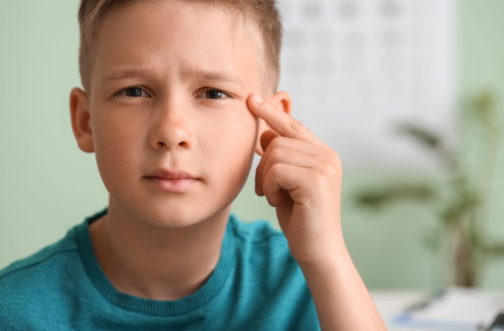 A child pointing to their left eye and squinting slightly while looking at something in the distance.