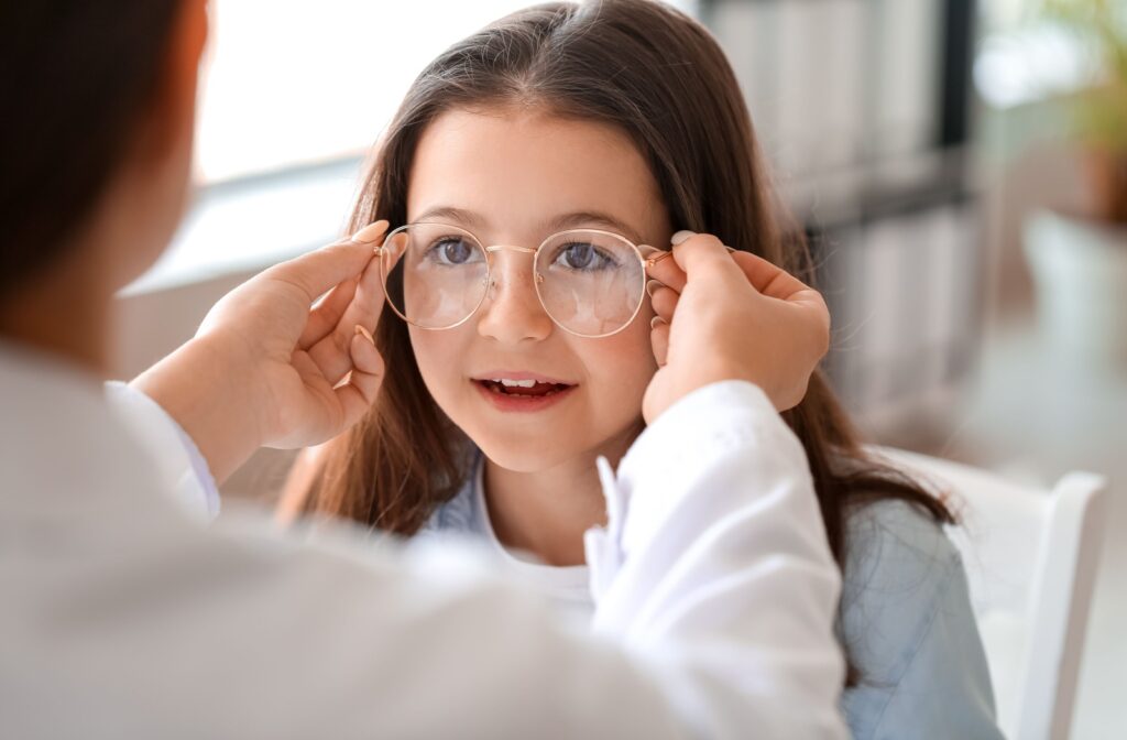 A close-up image of an eye doctor placing eyeglasses on a child's face.